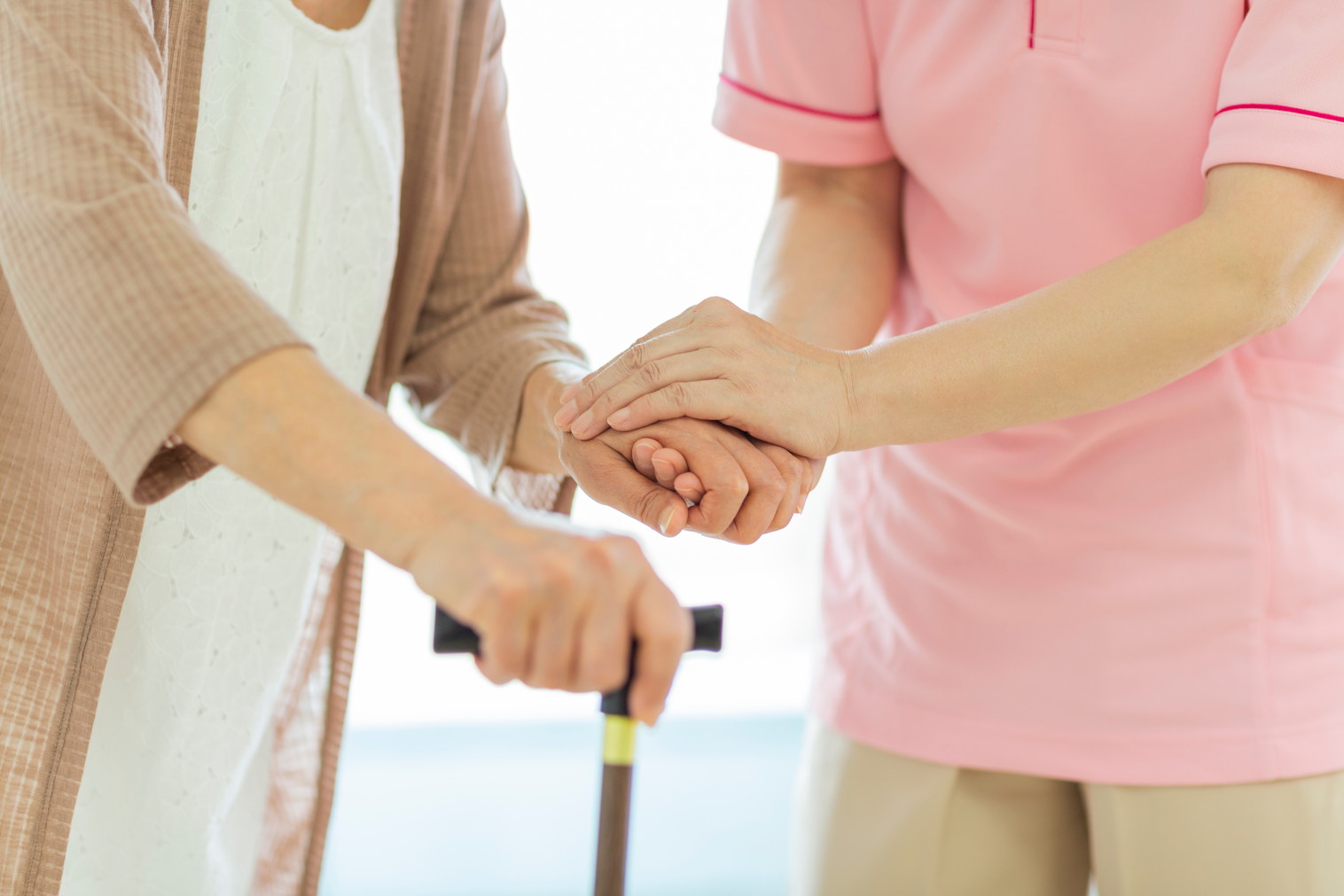 杖をついて歩く女性とサポートする女性の写真